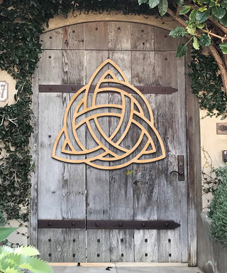 a wooden door with a large Celtic knot design hanging on it, surrounded by greenery.