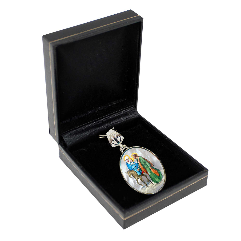 A black jewelry box containing a silver pendant with a religious scene depicted on it.