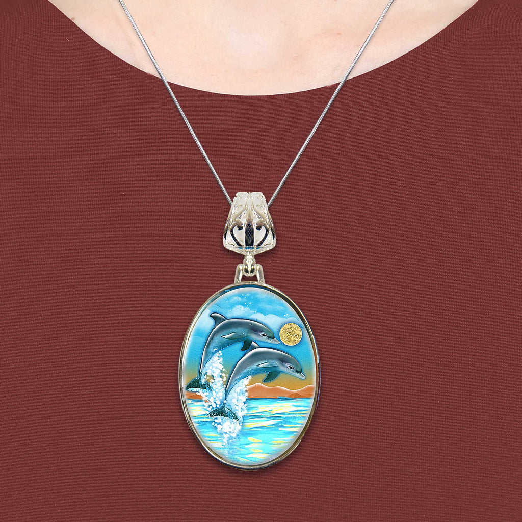 A necklace with a pendant featuring a painting of two dolphins jumping out of the water.