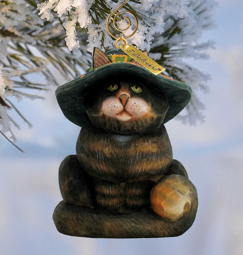 A wooden ornament in the shape of a cat wearing a green hat with a gold tag, hanging from a tree branch.