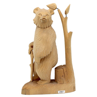 A wooden carving of a bear standing on a tree stump, holding a stick and leaf.