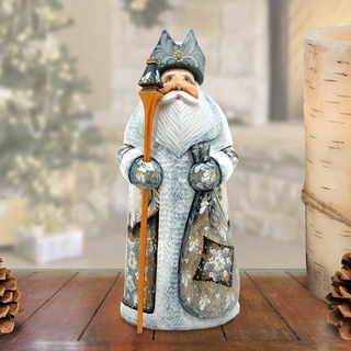 A figurine of Santa Claus holding a reindeer and a sack of presents, standing on a wooden surface with pine cones in the background.