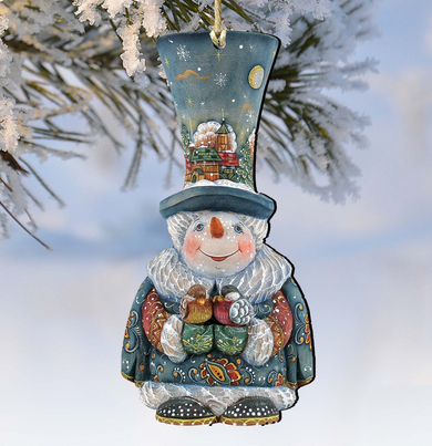 A snowman ornament with a blue hat and a snowy landscape on top, hanging on a tree branch.