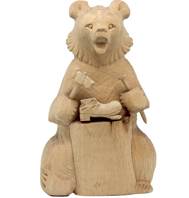 A wooden carving of a bear sitting on a wooden block, holding a small wooden object in its paws.