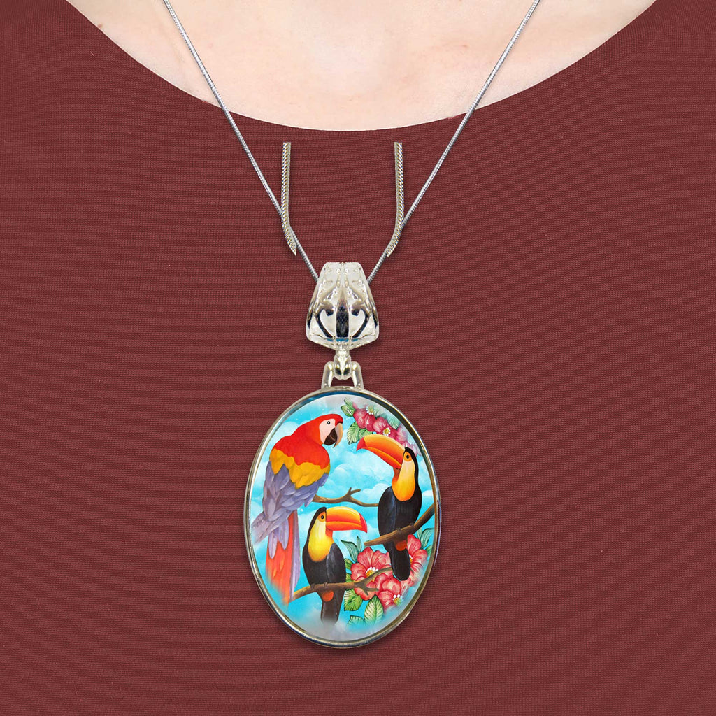 A necklace with a pendant featuring a colorful painting of three toucans perched on branches with flowers.