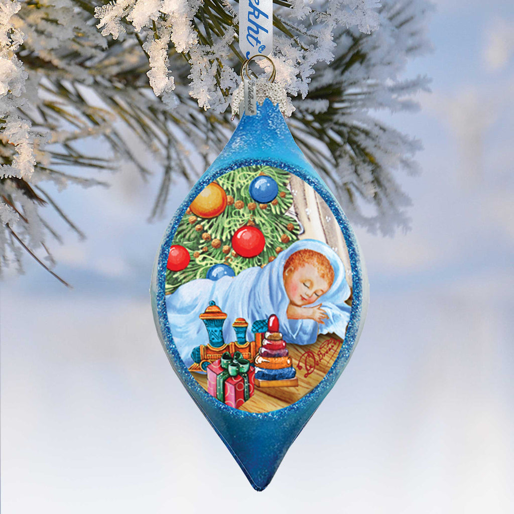 A blue ornament with a picture of a sleeping baby and Christmas decorations hanging on a tree branch.