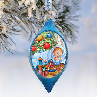 A blue ornament with a picture of a sleeping baby and Christmas decorations hanging on a tree branch.