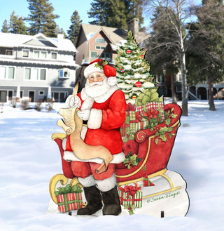 A cardboard cutout of Santa Claus sitting on a sled, surrounded by a Christmas tree and presents, with a snowy background.