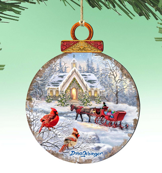A round ornament depicting a snowy winter scene with a church, a horse-drawn sleigh, and two red cardinals perched on a tree branch.