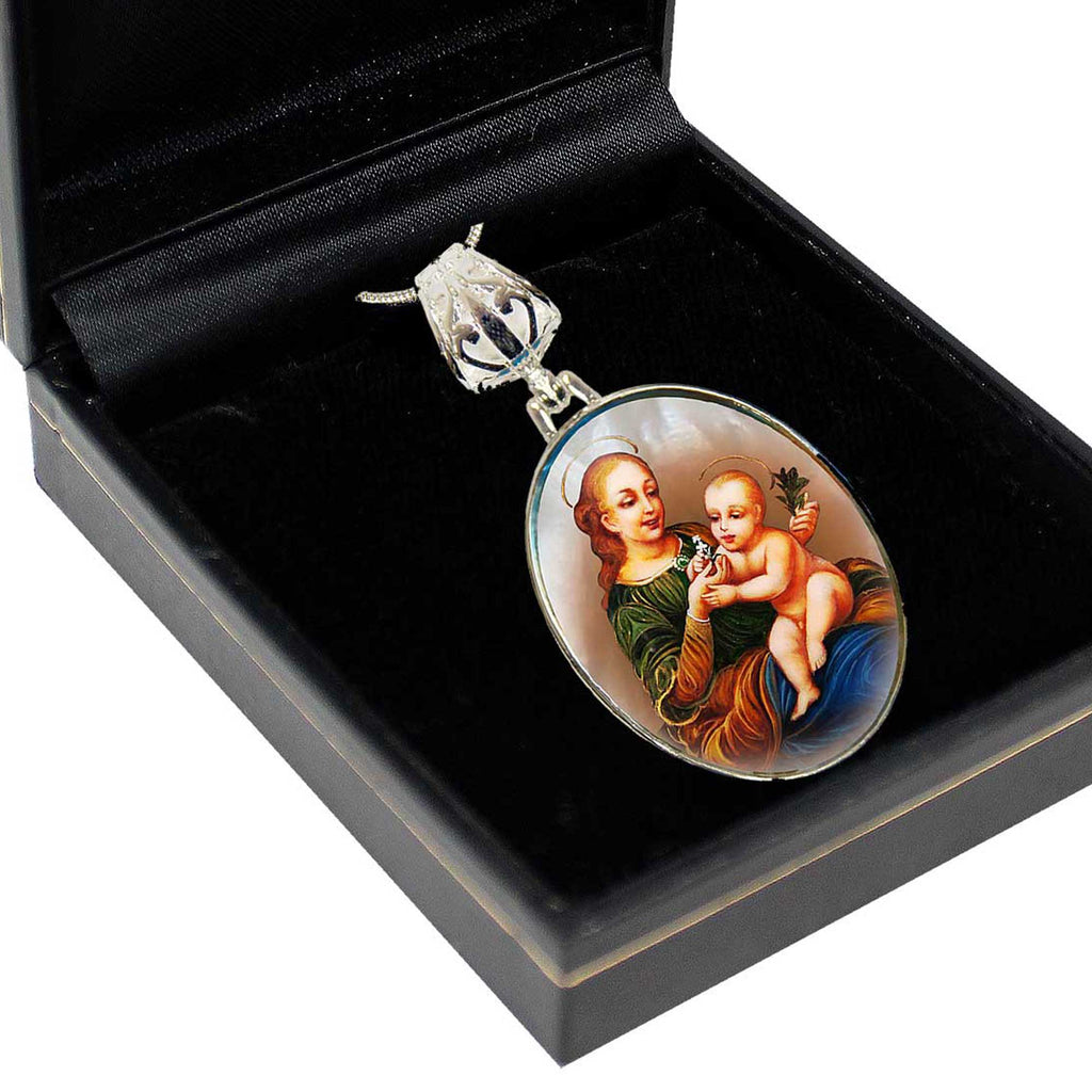 A pendant with a religious scene featuring a woman holding a baby, displayed in a black box.