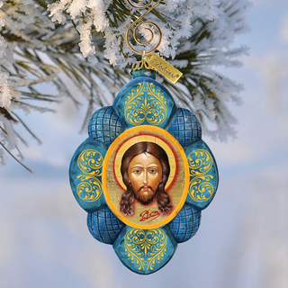 A blue and gold ornament featuring a depiction of Jesus Christ is hanging from a branch with snow on it.