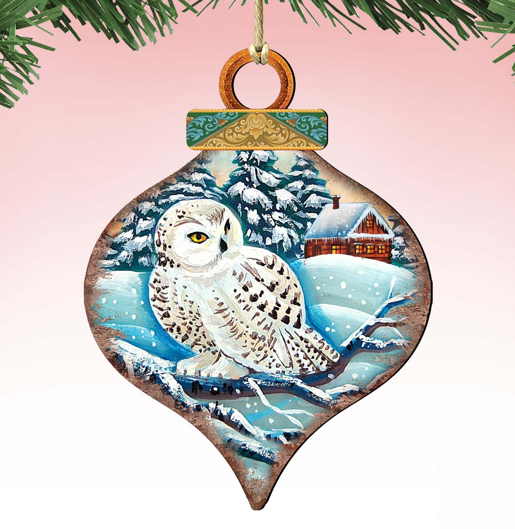 A wooden ornament in the shape of a snow owl, with a snowy landscape and a house in the background.