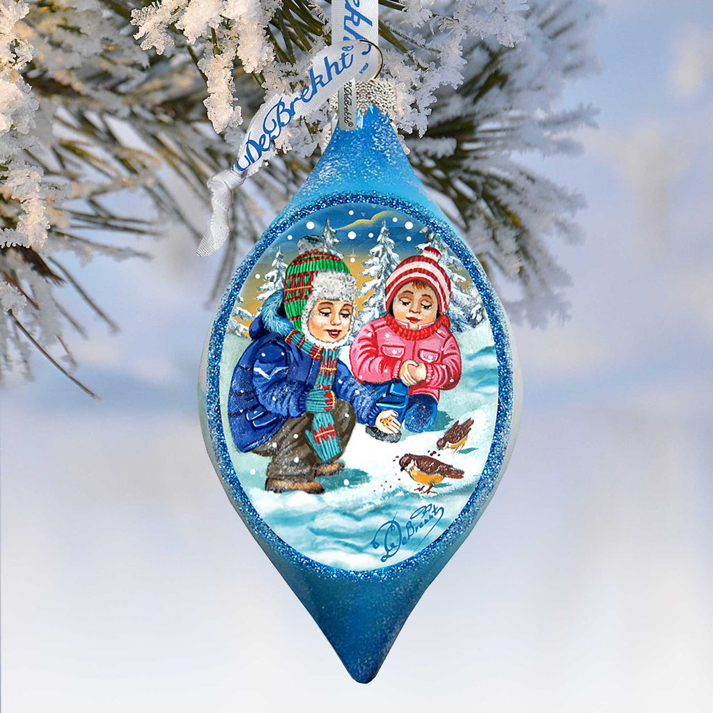 A blue ornament with a winter scene featuring two children playing in the snow, surrounded by snowflakes and birds.