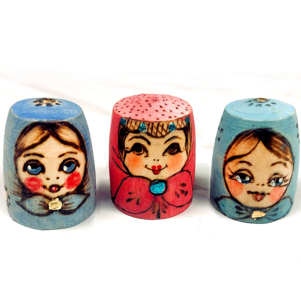 Three colorful, painted thimbles with faces on them, arranged in a row.