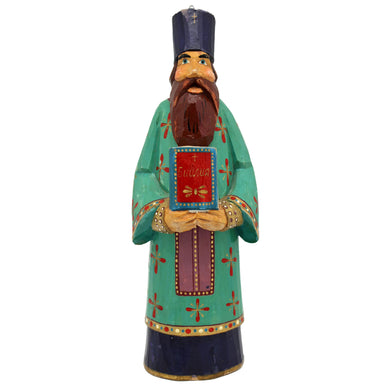 A colorful wooden statue of a bearded man wearing a green robe with red and gold accents, holding a book and standing against a white background.