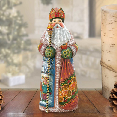 A colorful, hand-painted figurine of a saint or religious figure, wearing a long robe and holding a staff, stands on a wooden surface.