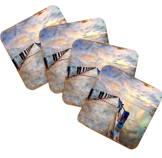a collection of four square coasters, each featuring a different painting of a beach scene. The coasters display various elements of the beach, such as a pier, a cloudy sky, and a sunset. The coasters are arranged in a row, with each one slightly overlapping the one before it, creating a layered effect. The paintings on the coasters depict a serene and picturesque beach landscape, capturing the essence of a relaxing day by the ocean.