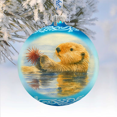 A blue ornament with a painting of an otter swimming in the water, hanging on a tree branch.