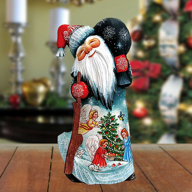 A wooden Santa Claus figurine with a white beard and red hat, holding a red ornament, stands on a wooden surface against a blurred background of Christmas decorations.