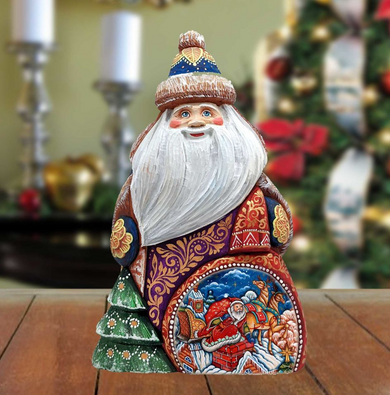 A wooden Santa Claus figurine with intricate decorations and a painted Christmas tree in the background.