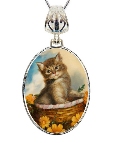 A silver pendant necklace with a round oval-shaped frame that contains a painting of a kitten sitting in a basket filled with flowers.