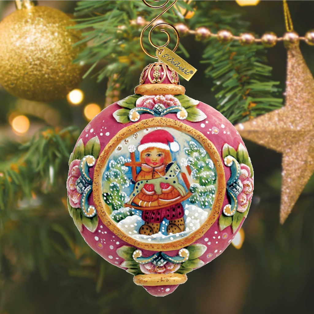A pink ornament with a Christmas tree and a gold star ornament in the background.