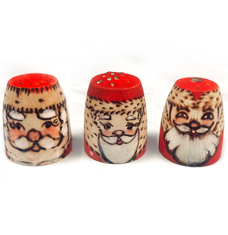 Three wooden objects with painted faces, each depicting a different Santa Claus character.