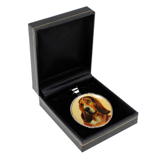 A pendant in the shape of a dog's head is displayed in a black jewelry box.