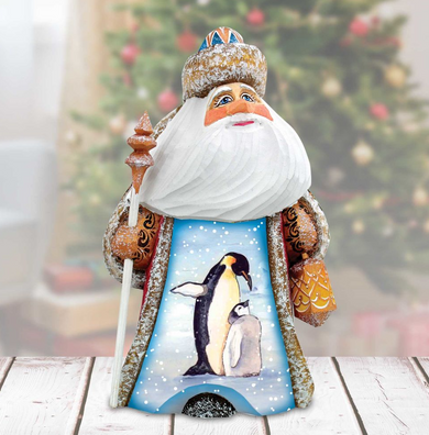 A wooden Santa Claus figurine with a penguin design on its chest, standing on a wooden surface.
