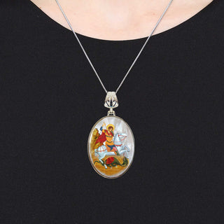 A silver necklace with a pendant featuring a religious scene.