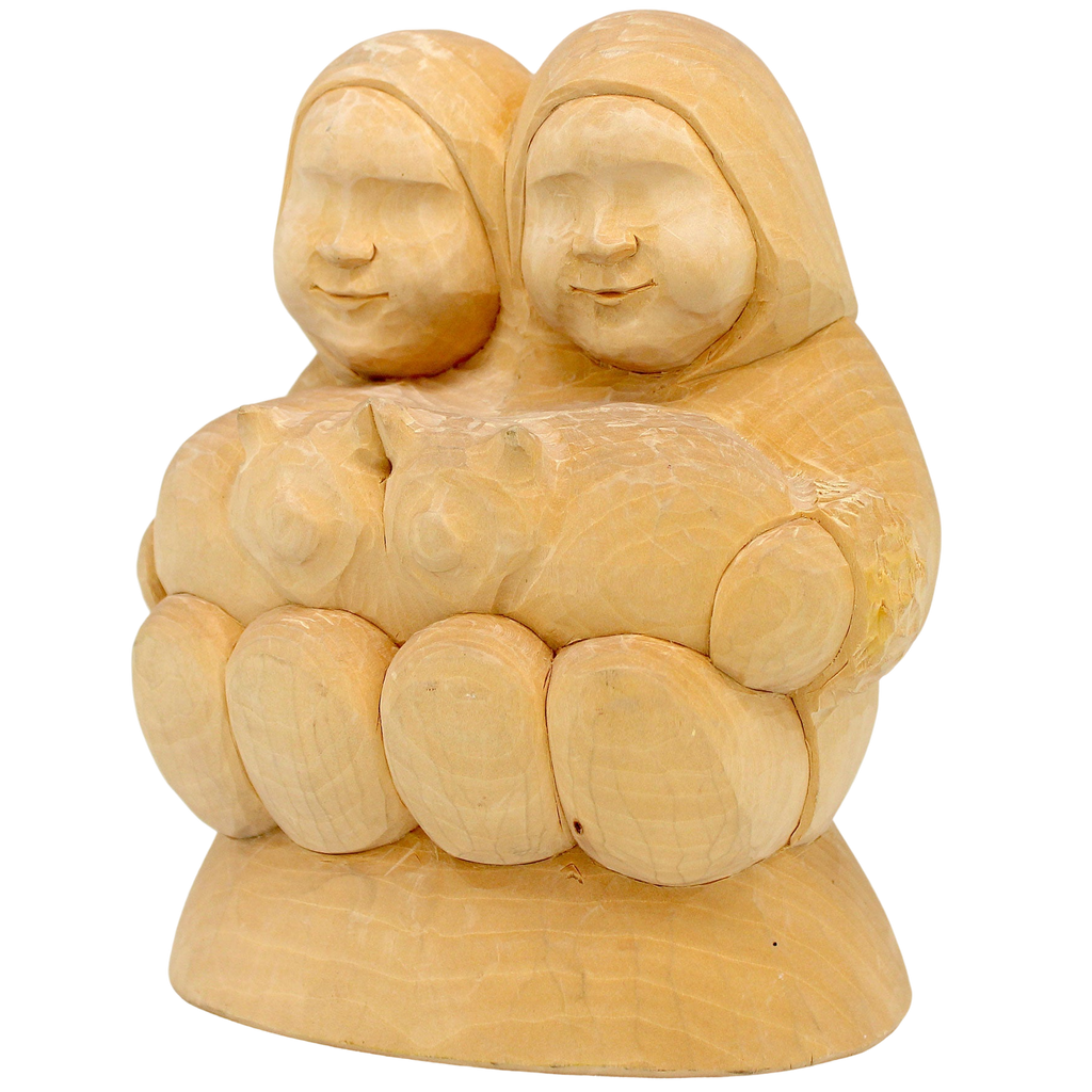 A wooden sculpture depicting two women holding a cat.