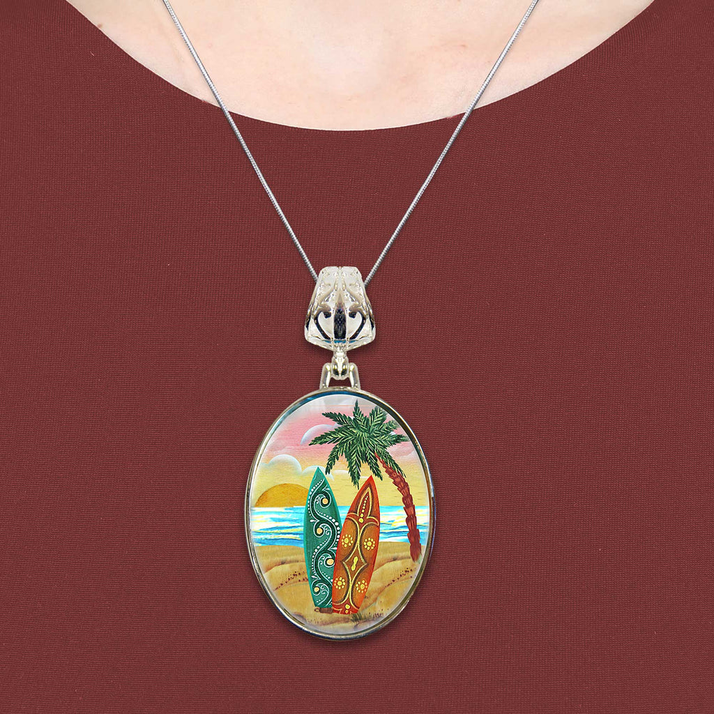 A necklace with a circular pendant featuring a beach scene with two surfboards and palm trees.