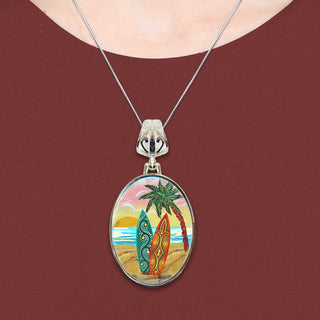 A necklace with a circular pendant featuring a beach scene with two surfboards and palm trees.