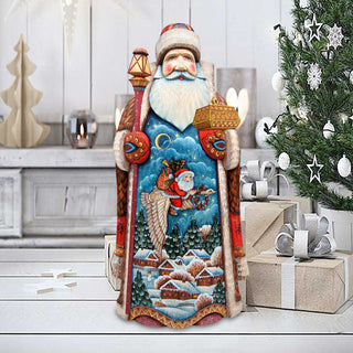 A large, colorful Christmas ornament depicting Santa Claus holding a lantern and a basket of presents, standing in front of a decorated Christmas tree.