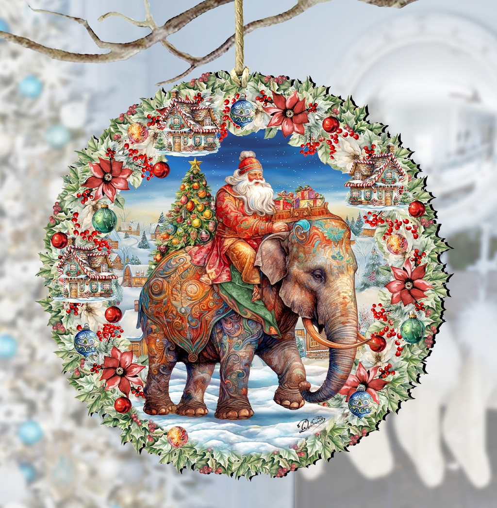 A decorative ornament featuring a large elephant carrying a person on its back, surrounded by a wreath of flowers and a Christmas tree. Santa Claus is riding the elephant, and the scene appears to be set in a snowy landscape.