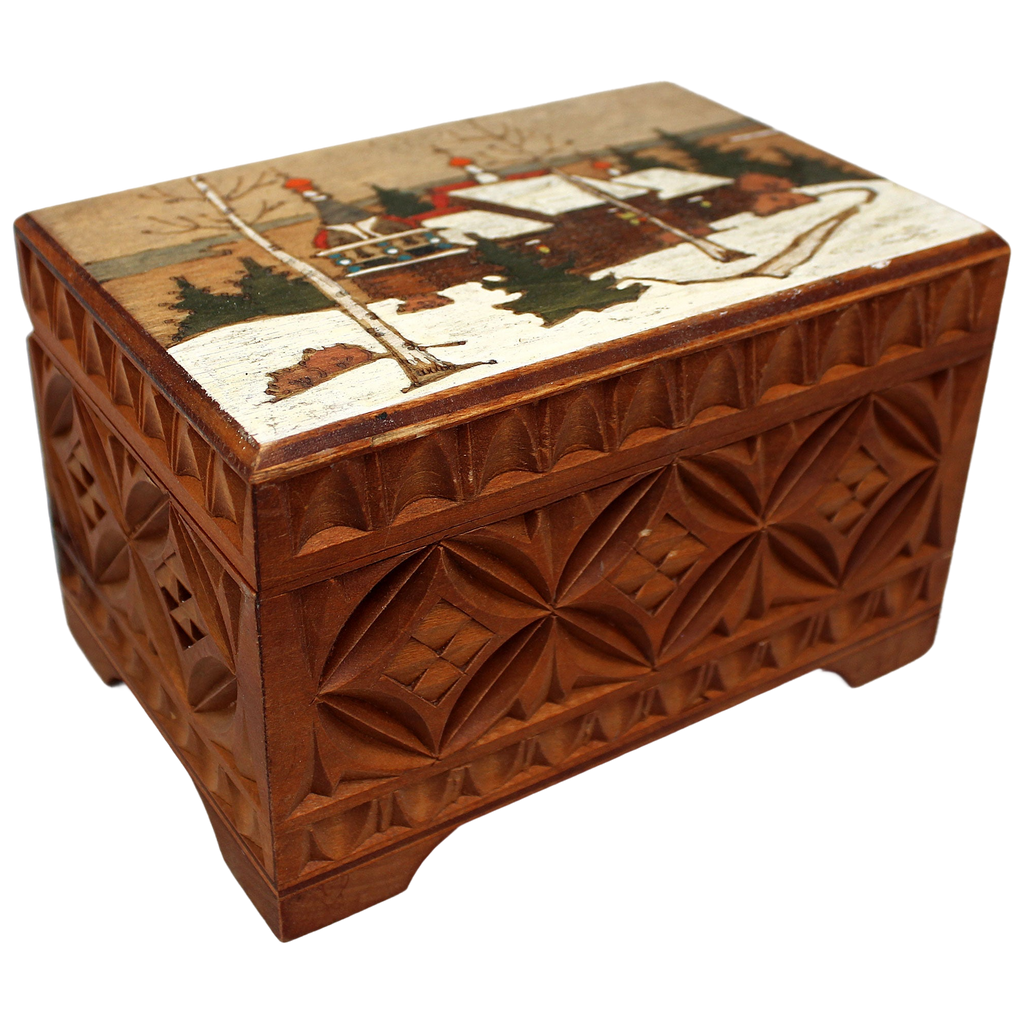 A wooden box with a carved design depicting a winter landscape with a village and trees.