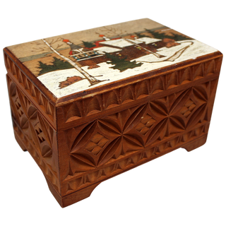 A wooden box with a carved design depicting a winter landscape with a village and trees.