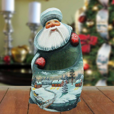 A wooden Santa Claus figurine with a white beard and hat, holding a red ornament, is displayed on a wooden surface against a blurred background of a Christmas tree and other holiday decorations.