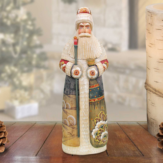 A figurine of Santa Claus is displayed on a wooden surface, with a blurred background that includes a Christmas tree and pine cones.