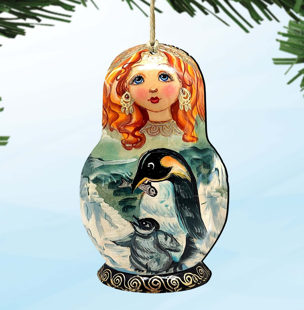 A decorative ornament featuring a painted doll with red hair and a golden crown, along with a painted penguin and a landscape scene.