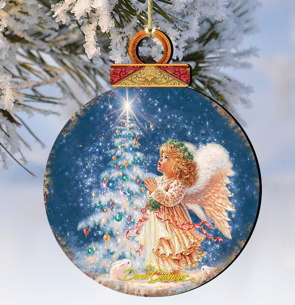 A round Christmas ornament featuring an angel with white wings and a golden robe, gazing up at a decorated Christmas tree.