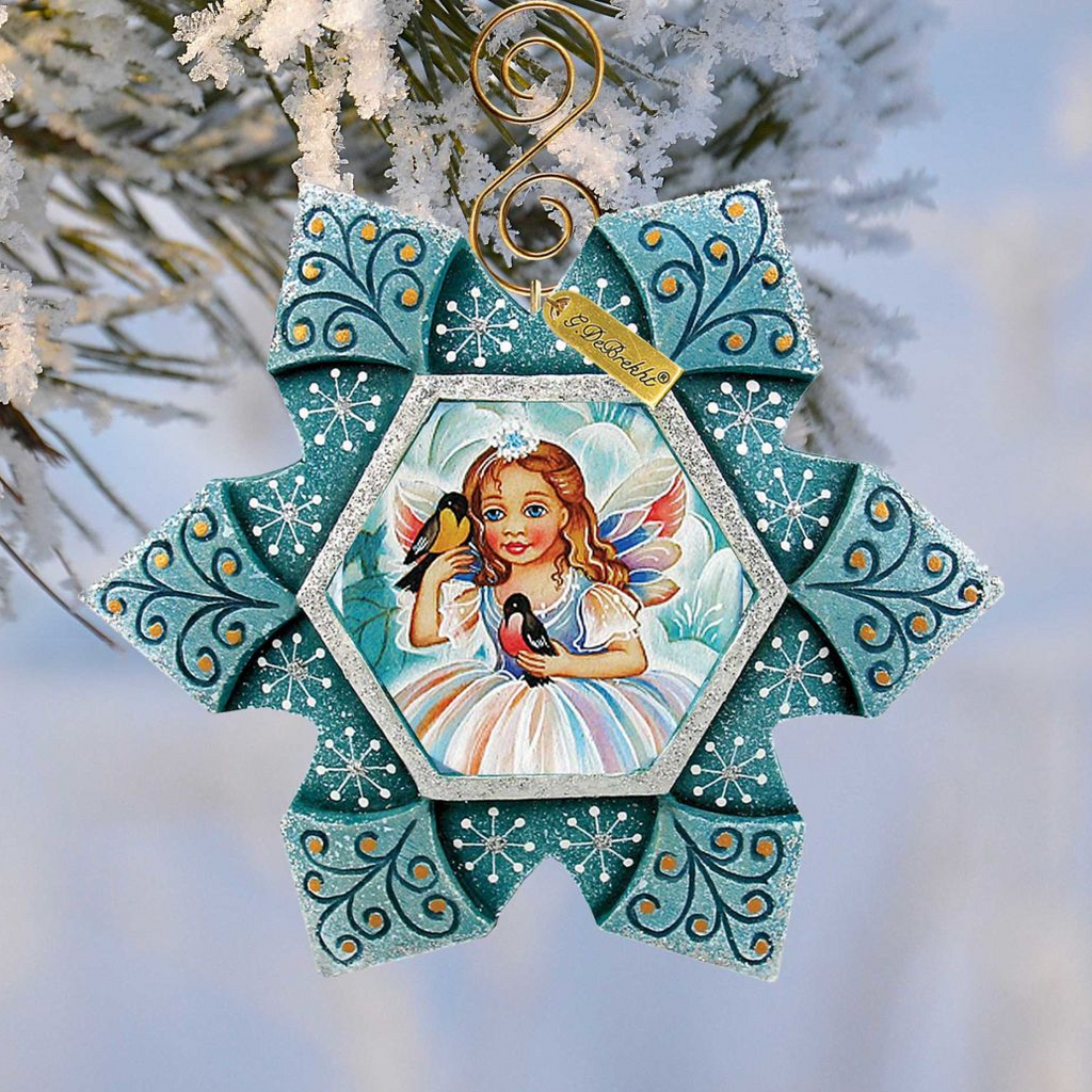 A decorative ornament featuring a fairy with a crown, surrounded by intricate blue and white patterns, hanging on a snowy branch.