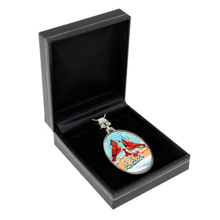 A pendant with a design of two red birds, possibly a cardinal, is displayed in a black jewelry box.