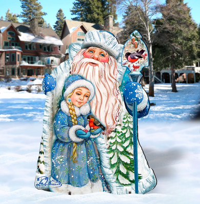 A large, colorful cardboard cutout of Santa Claus holding a young girl in a blue dress, with snow-covered trees in the background.