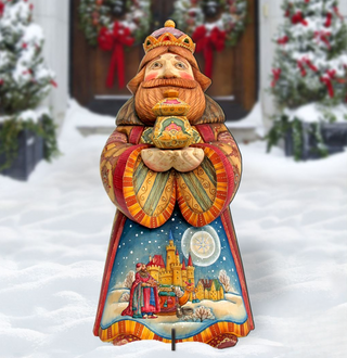A colorful wooden statue of a king or queen, holding a crown and a book, stands in the snow in front of a wreath-adorned door.
