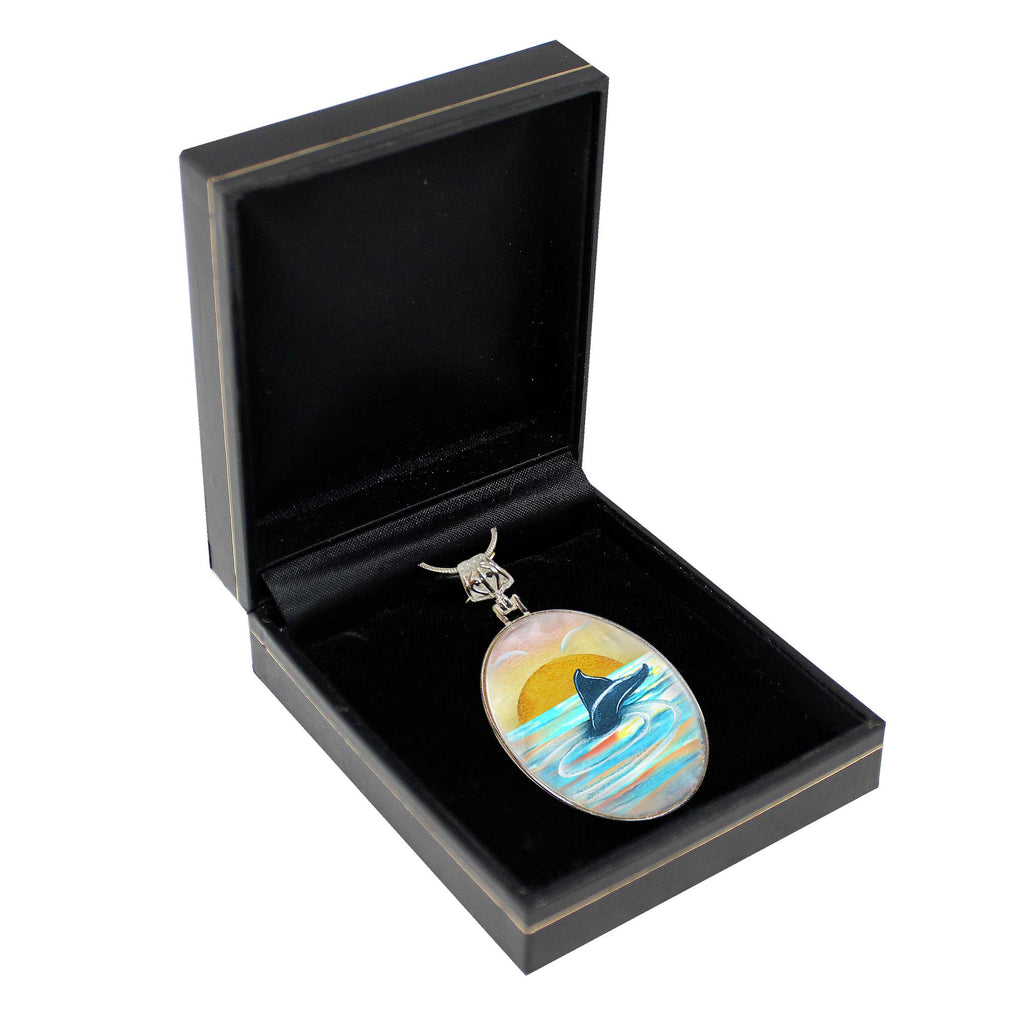 A pendant with a painting of a dolphin is displayed in a black jewelry box.