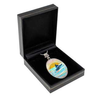 A pendant with a painting of a dolphin is displayed in a black jewelry box.