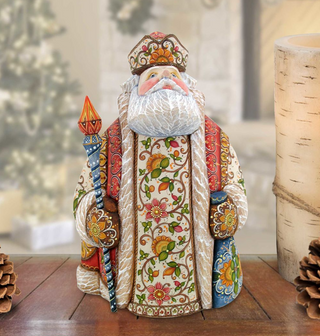 A colorful, intricately decorated figurine of Santa Claus holding a staff and a blue bag, placed on a wooden surface.