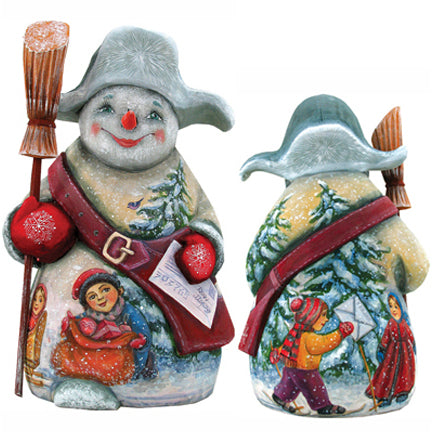 A snowman figurine with a red scarf and hat, holding a red ball and a newspaper, standing in a snowy landscape with a child and another person in the background.