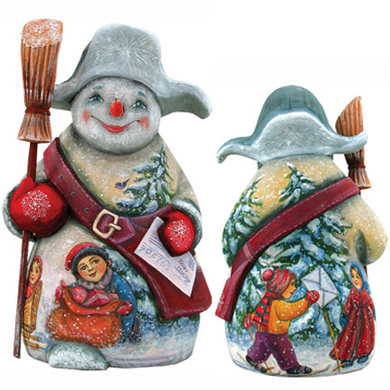 A snowman figurine with a red scarf and hat, holding a red ball and a newspaper, standing in a snowy landscape with a child and another person in the background.